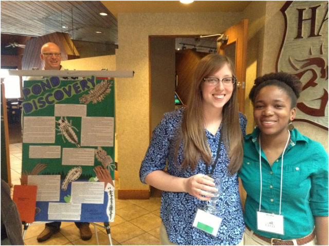 Interns Maddie and Mysha (from left) prepare for their poster presentations. Maddie’s poster outlines her lesson on discovering pond life. Photo Credit: Kate Lowry 
